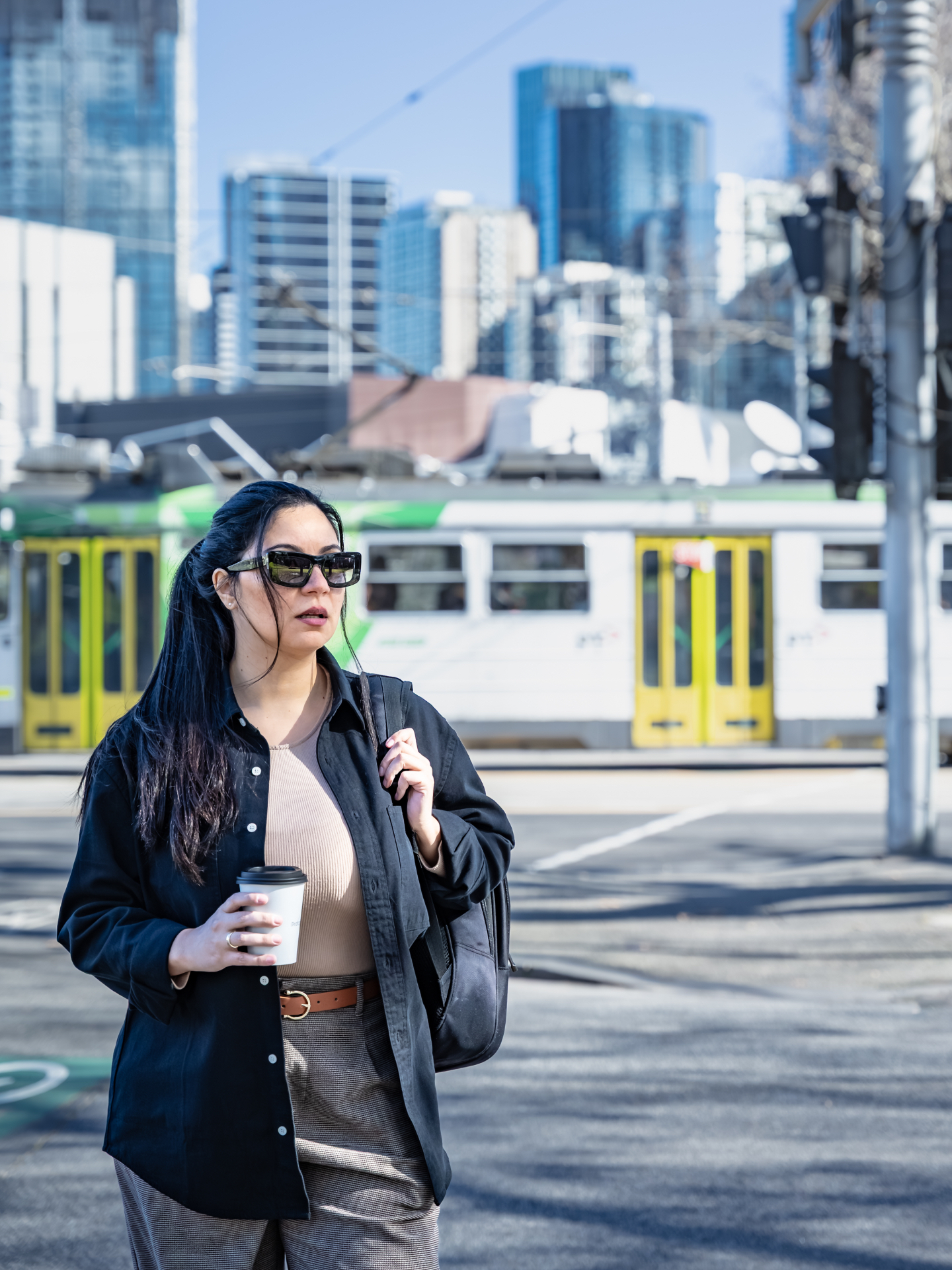 Woman holding a coffee cup with a Melbourne tram and city skyline behind her