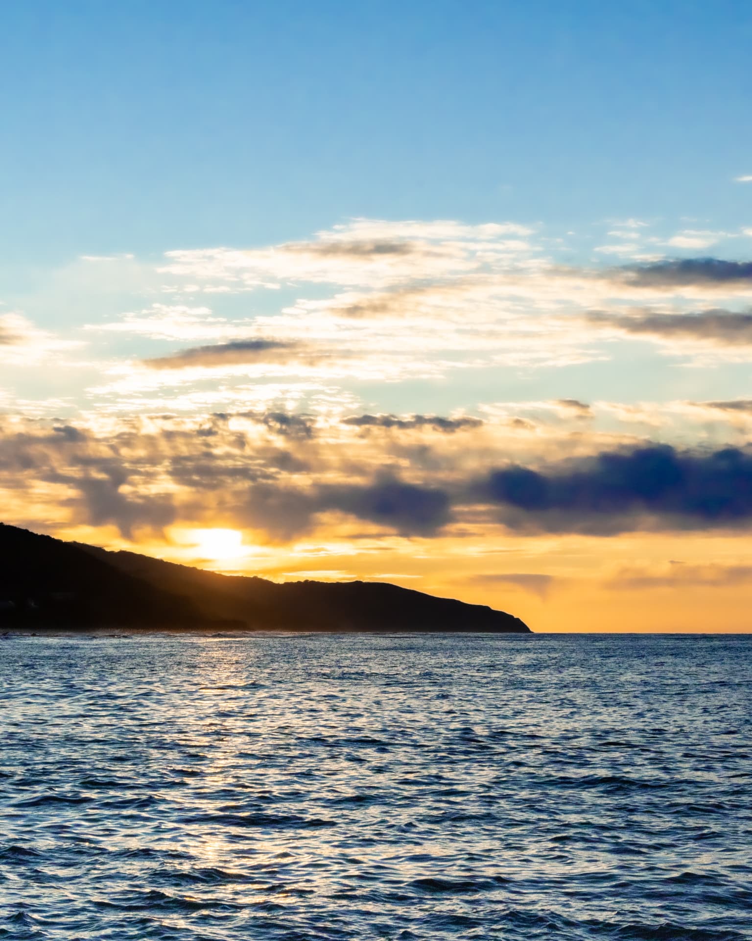 Sunrise over the ocean behind a coastal headland
