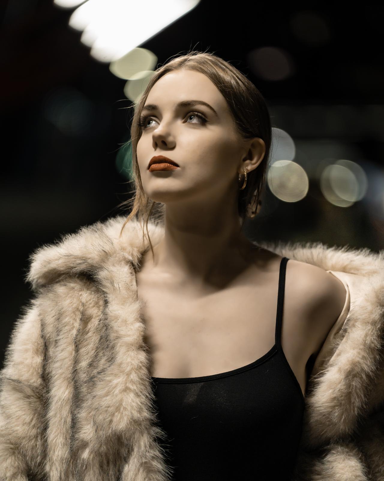 Night portrait of a woman in a fur coat lit by city bokeh