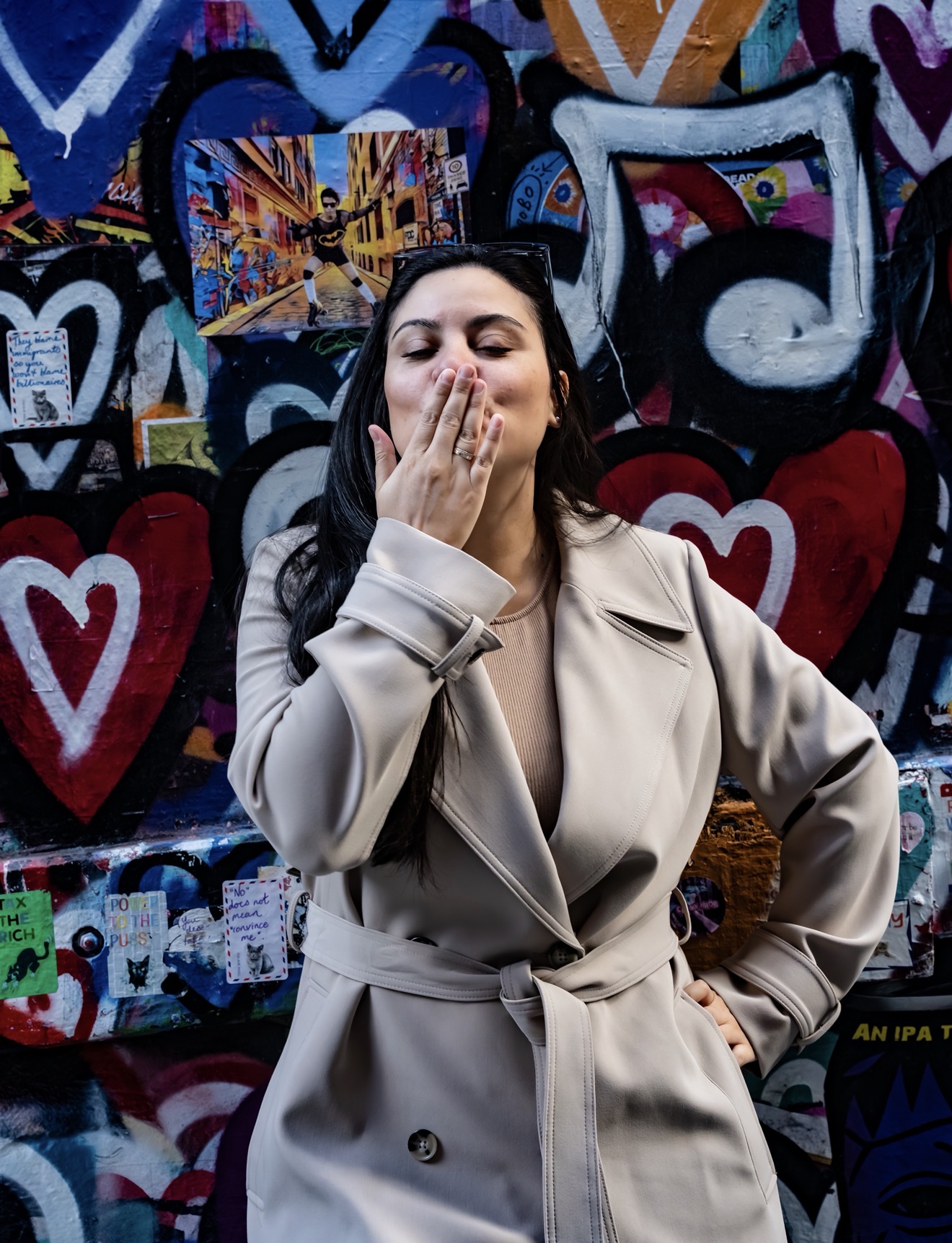 Woman in a trench coat blowing a kiss in front of colourful heart graffiti in a Melbourne laneway